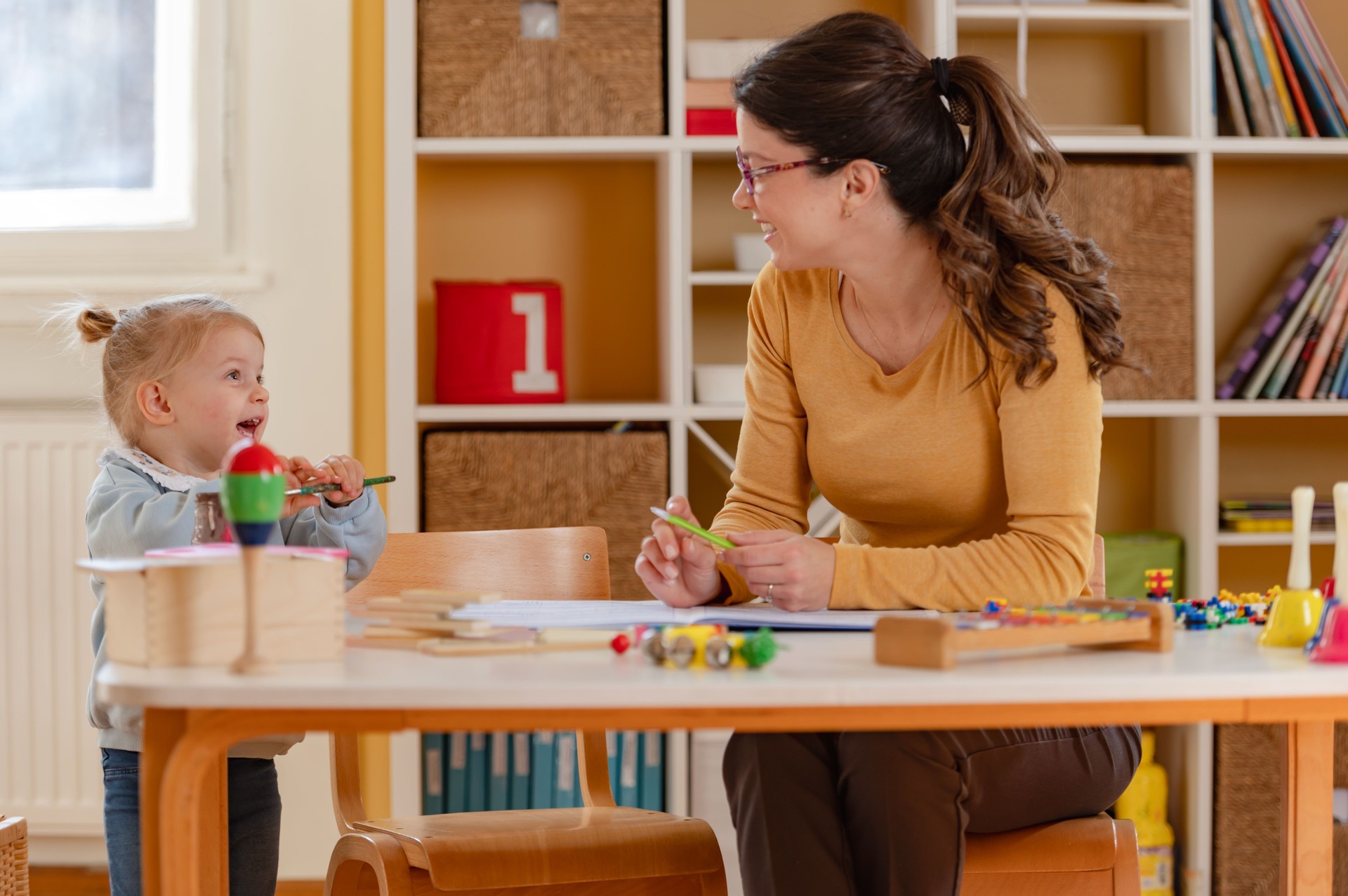 A young woman and a little girl engage in educational activities using colorful toys and building blocks, fostering creativity, learning, and bonding in a bright classroom setting